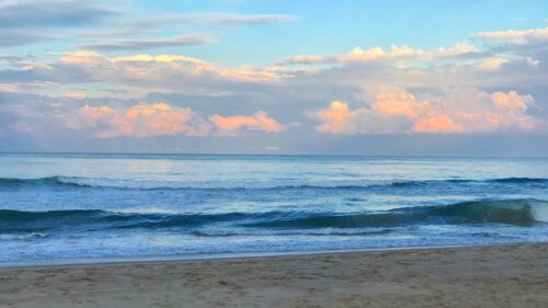Soft waves roll onto a sandy beach under pastel clouds.