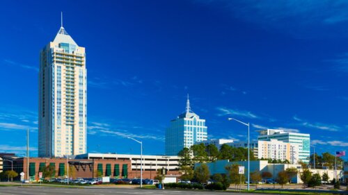Tall modern buildings rise against a bright blue sky.