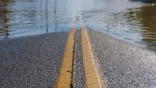 Water covers a road with yellow lines partially submerged.